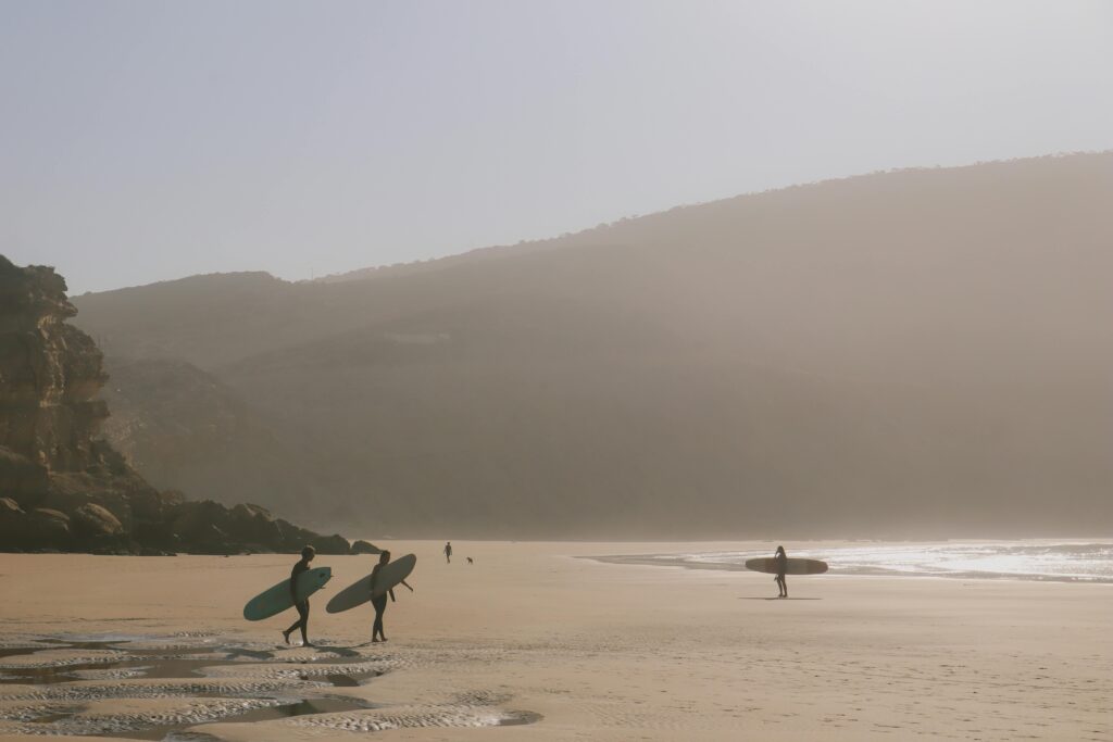 Surfers stroll along the serene Imsouane beach, Morocco, capturing a tranquil moment at sunset.