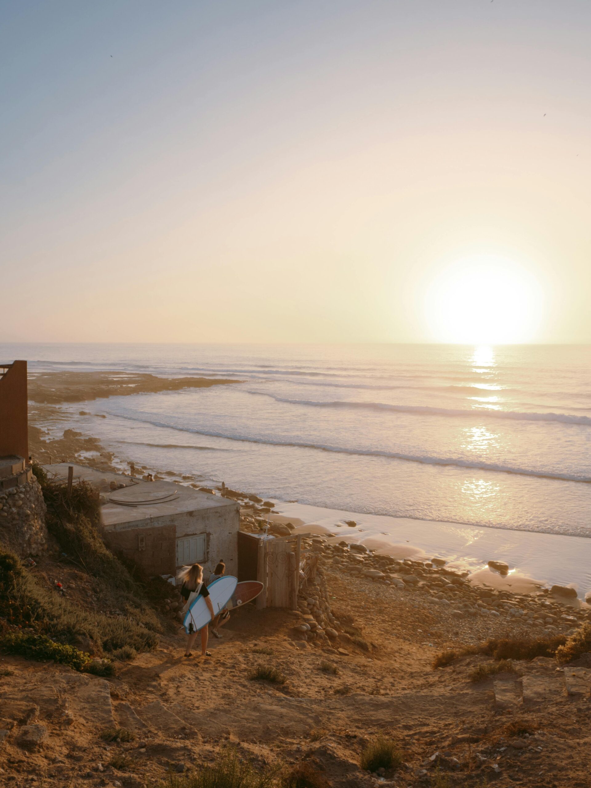 Surfer carrying board at sunset on Imsouane Beach, perfect ocean views.